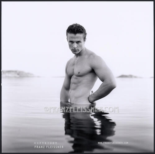 Attractive Swedish young shirtless athletic man standing in water looking at Hasselblad Camera